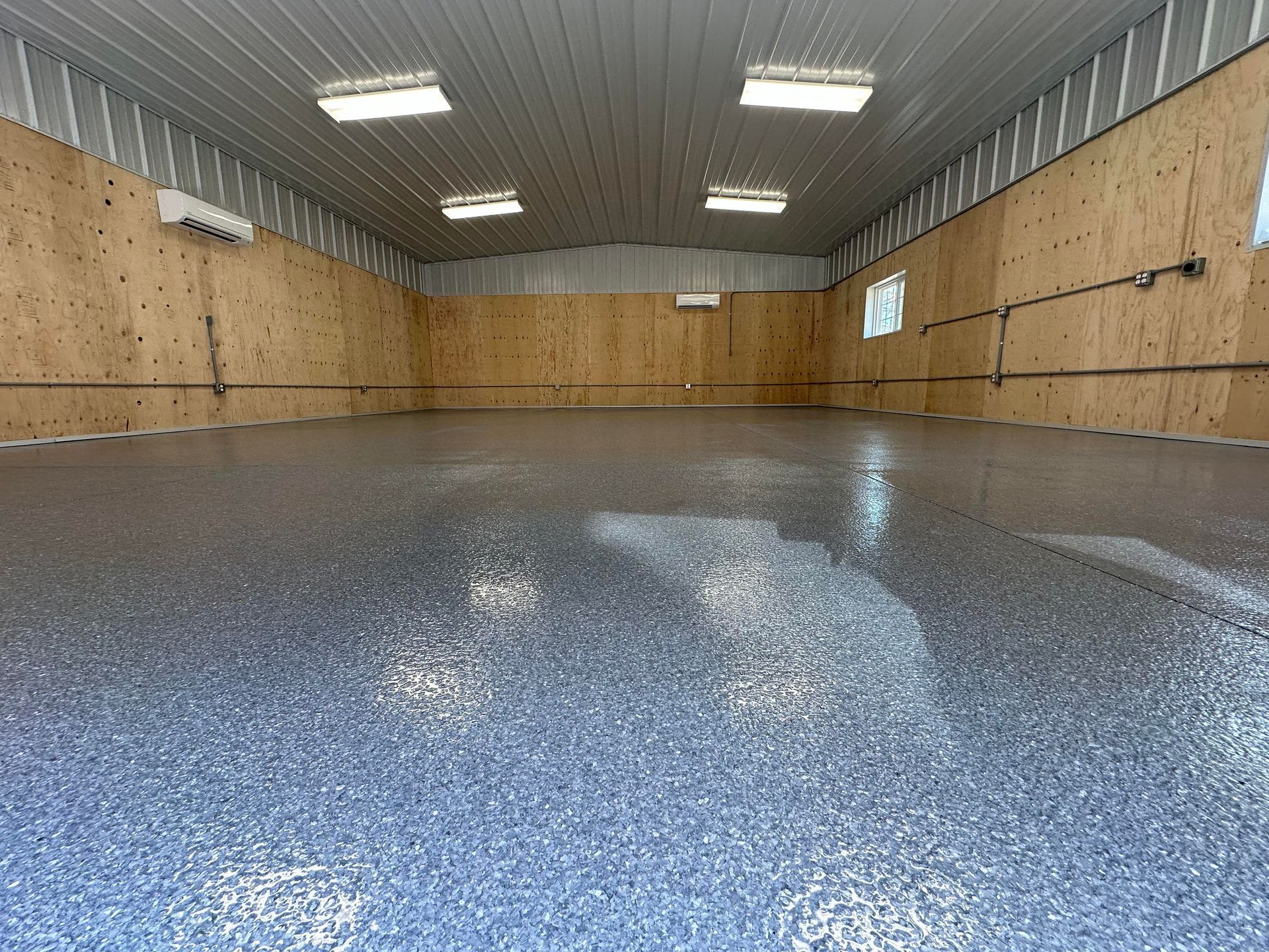 Empty indoor room with wood-paneled walls and a glossy speckled floor under ceiling lights