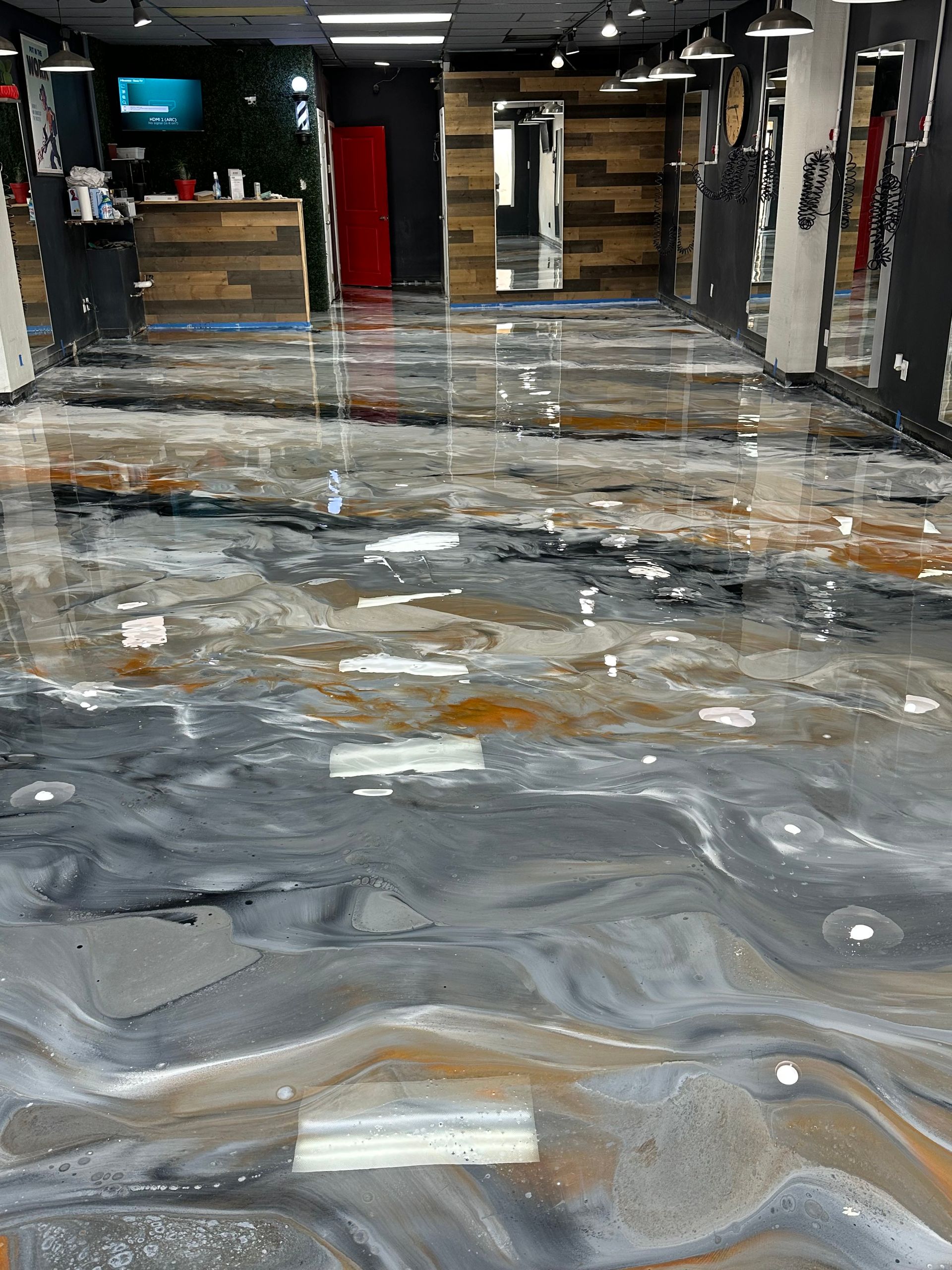 Polished gray-and-brown concrete floor in a modern hallway or lobby with wood-paneled walls and red doors