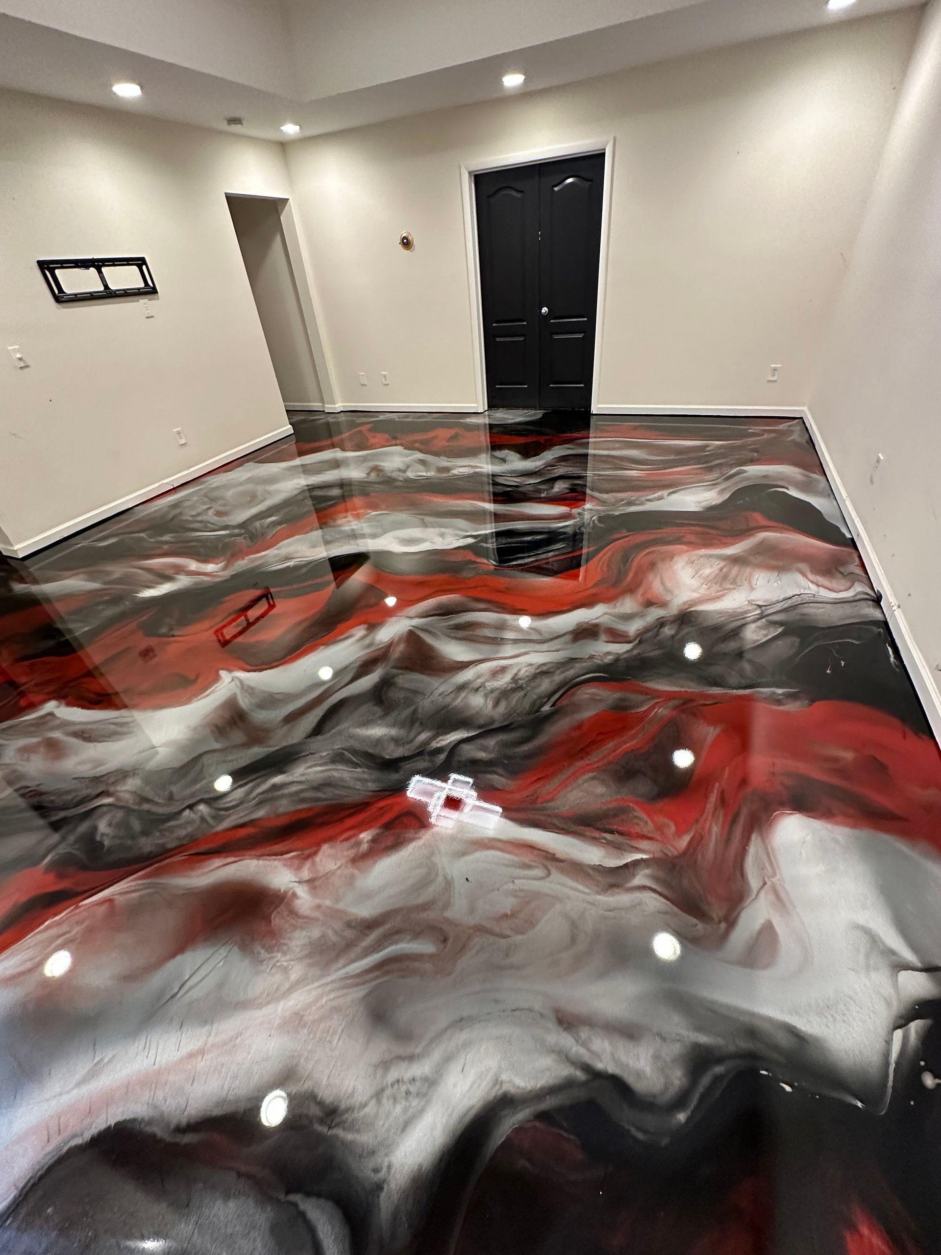 Abstract red, black, and white swirled floor finish in an empty room with a black door.