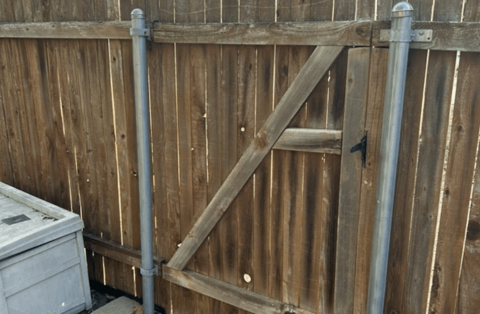 Wooden gate in a brown wooden fence, supported by silver posts.