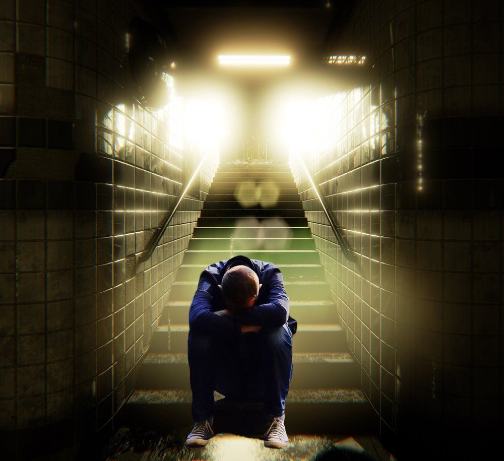a young man sits at the bottom of the stairs with head on arms crossed over his knees