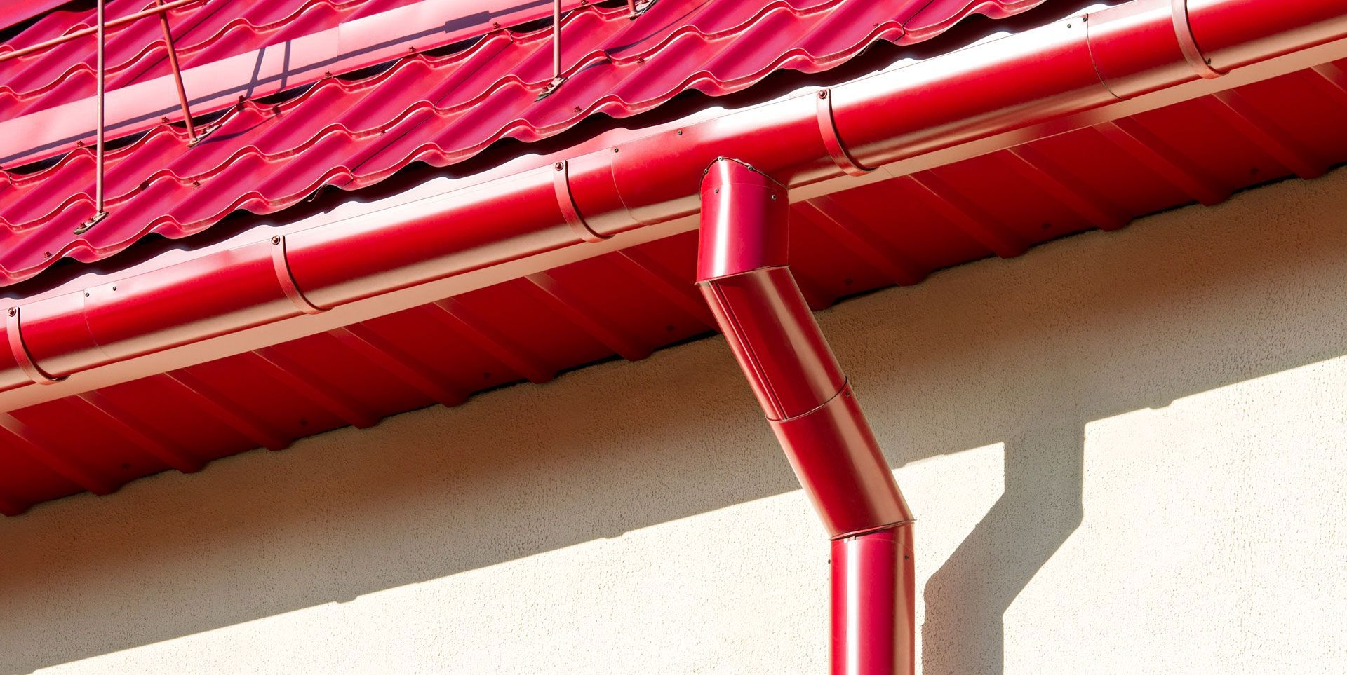 A red gutter on the side of a building with a red roof.