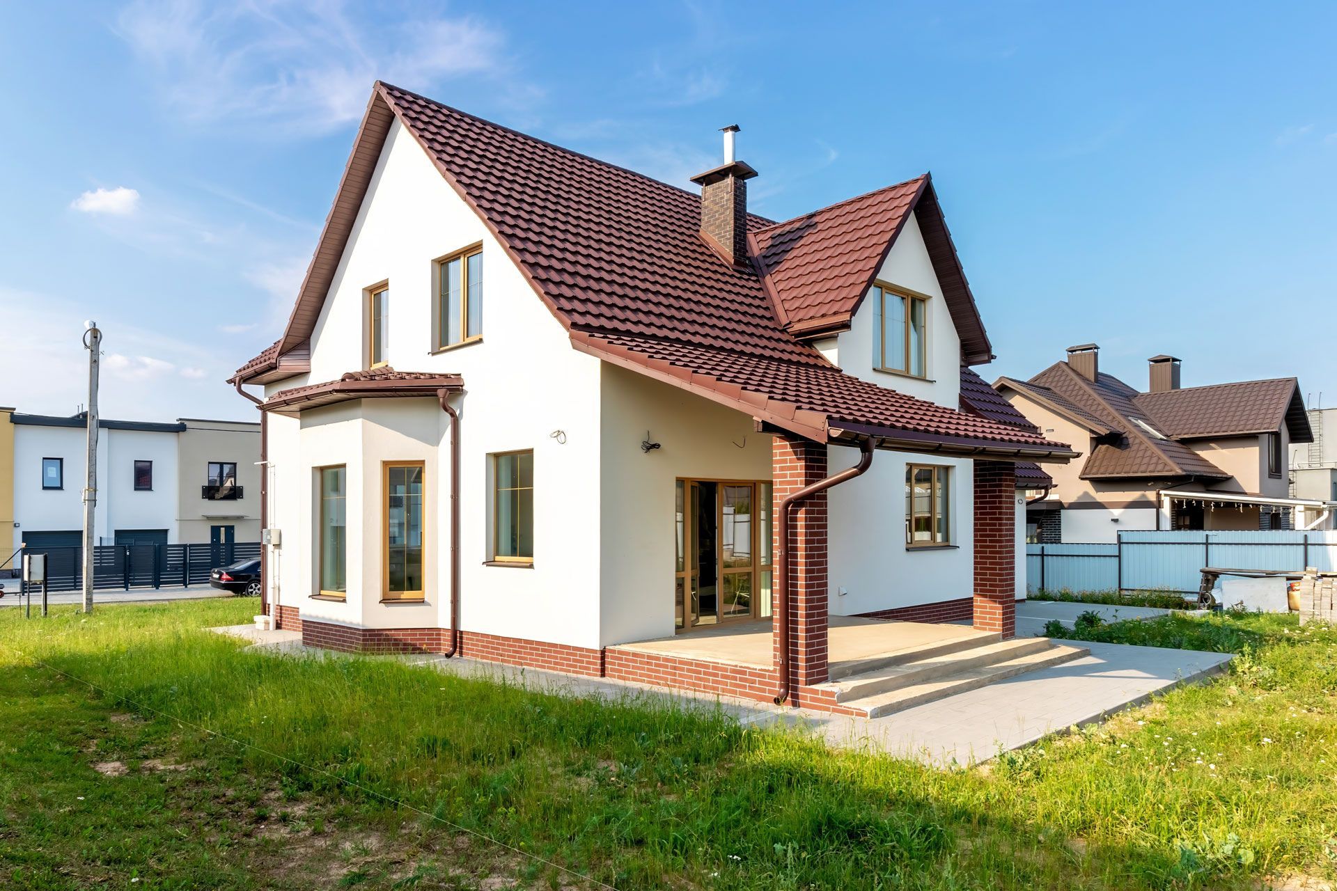 A white house with a brown roof is sitting on top of a lush green field.