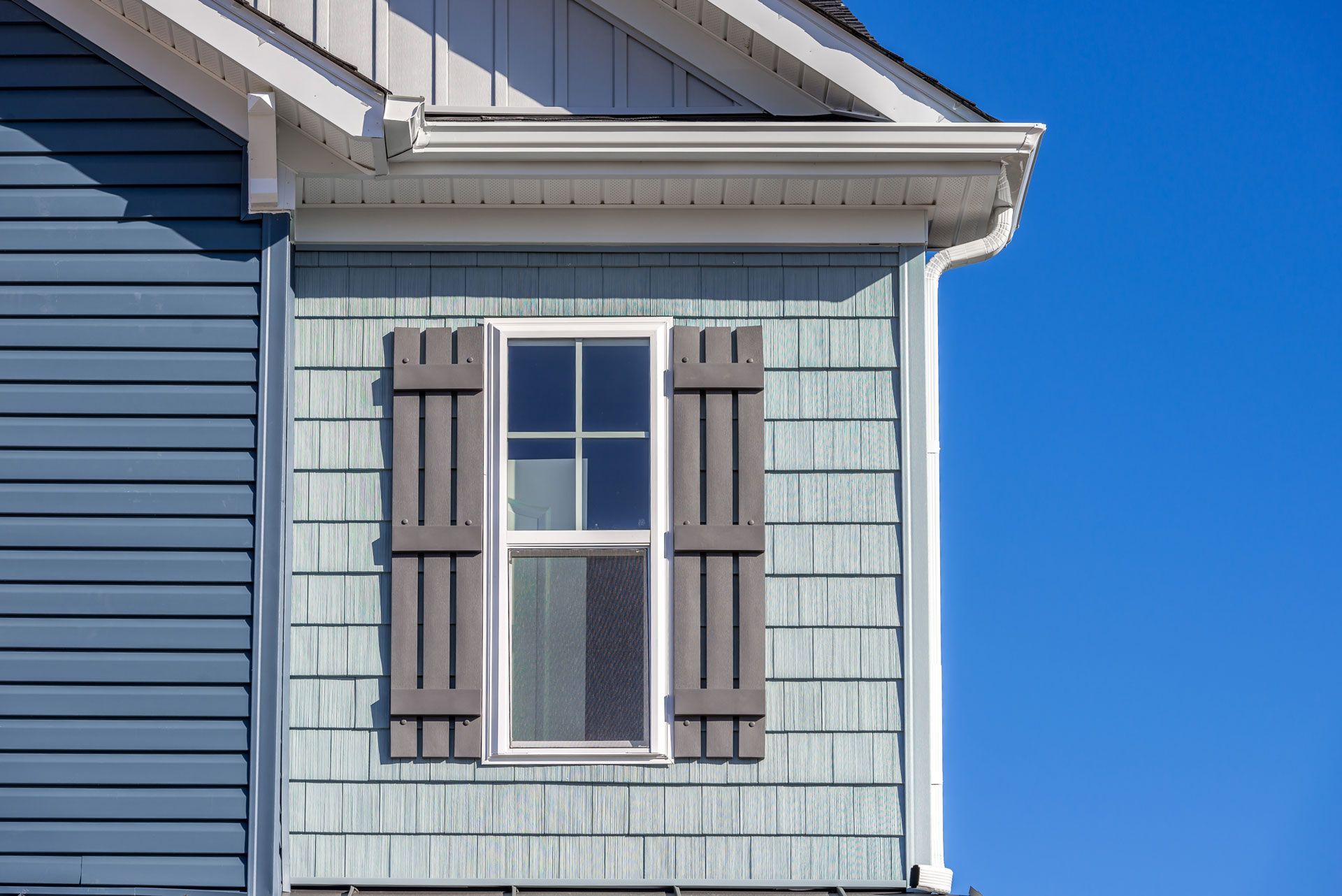 The side of a house with a window and shutters on it.