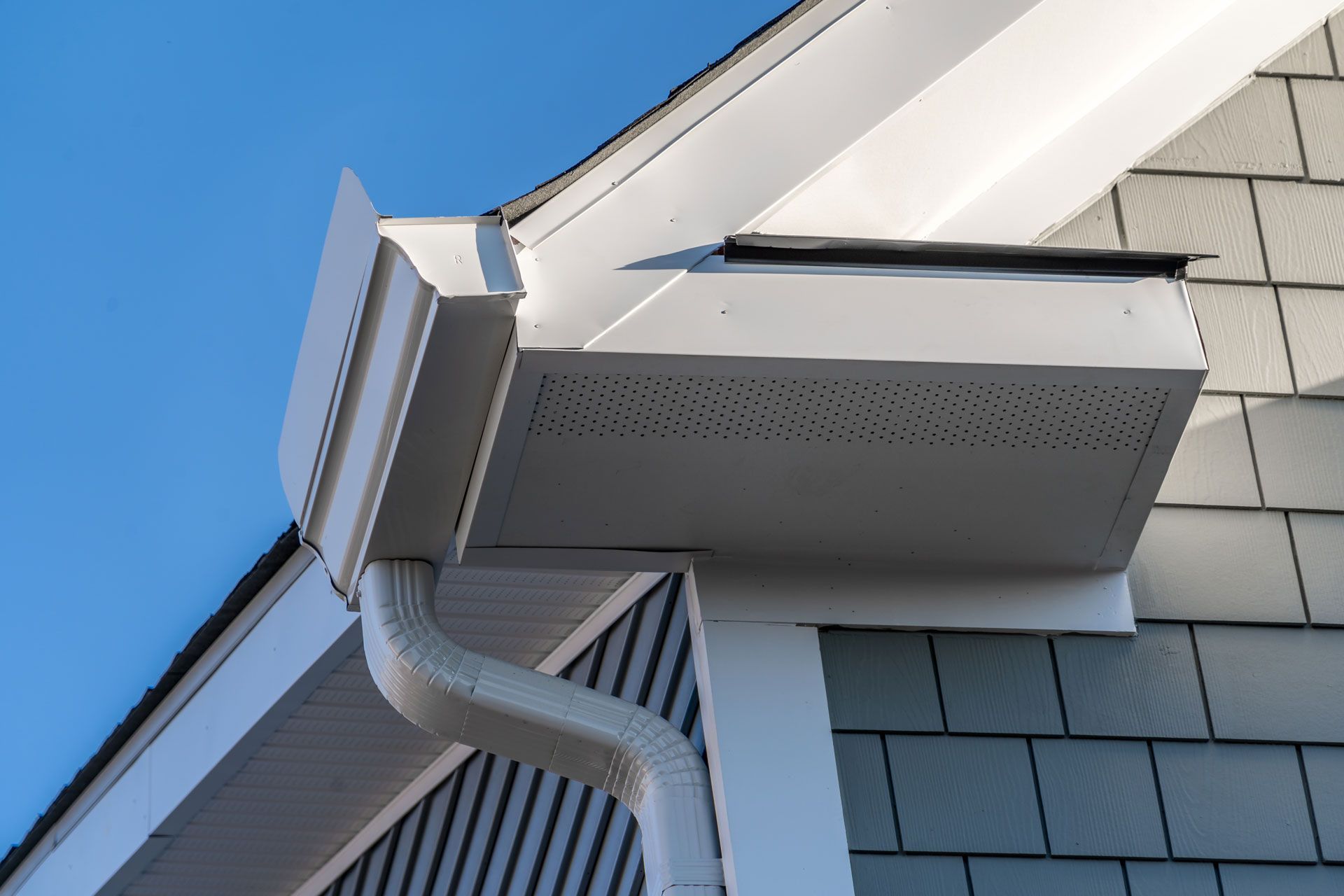 A white gutter on the side of a house with a blue sky in the background.