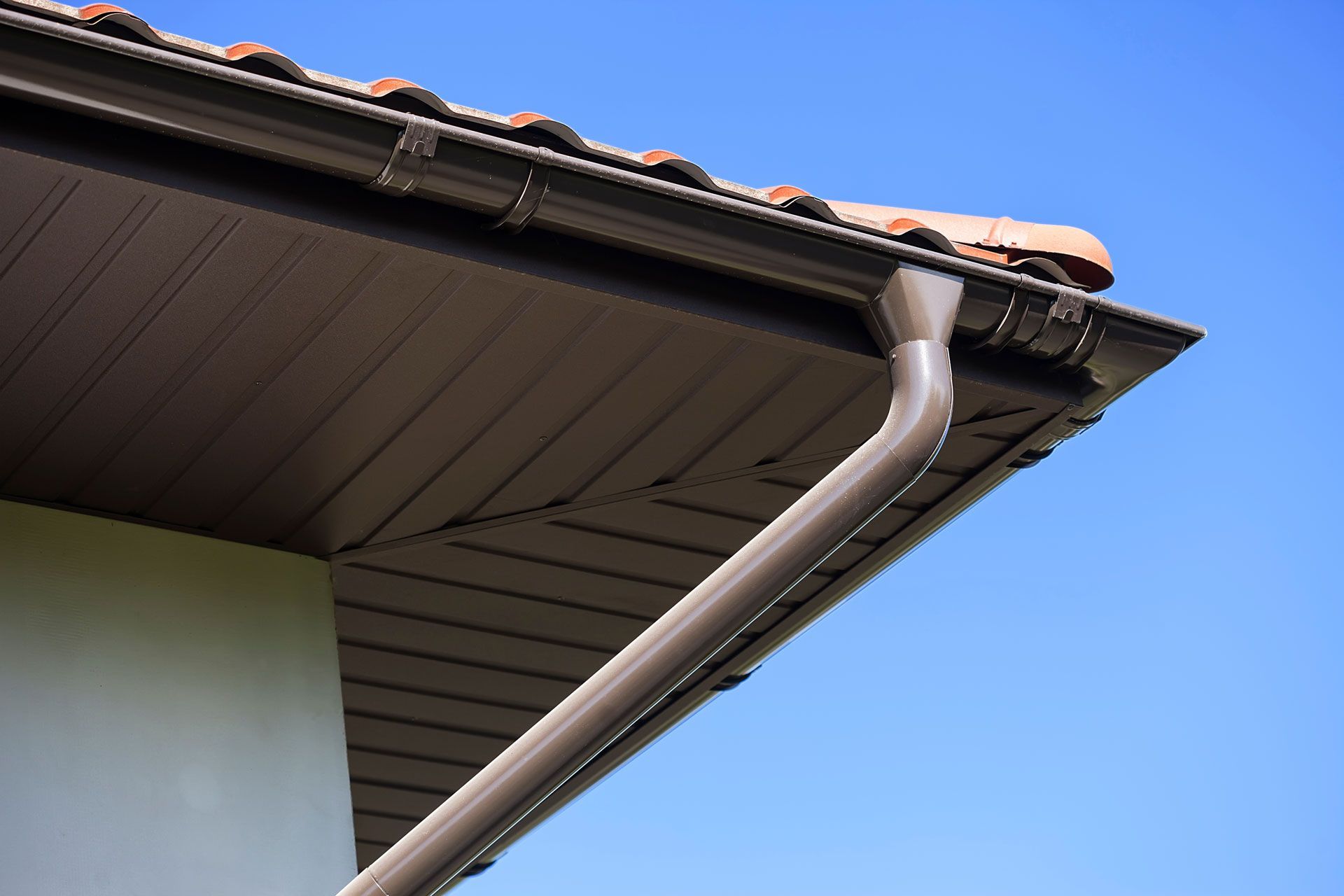 A gutter on the side of a house with a blue sky in the background.
