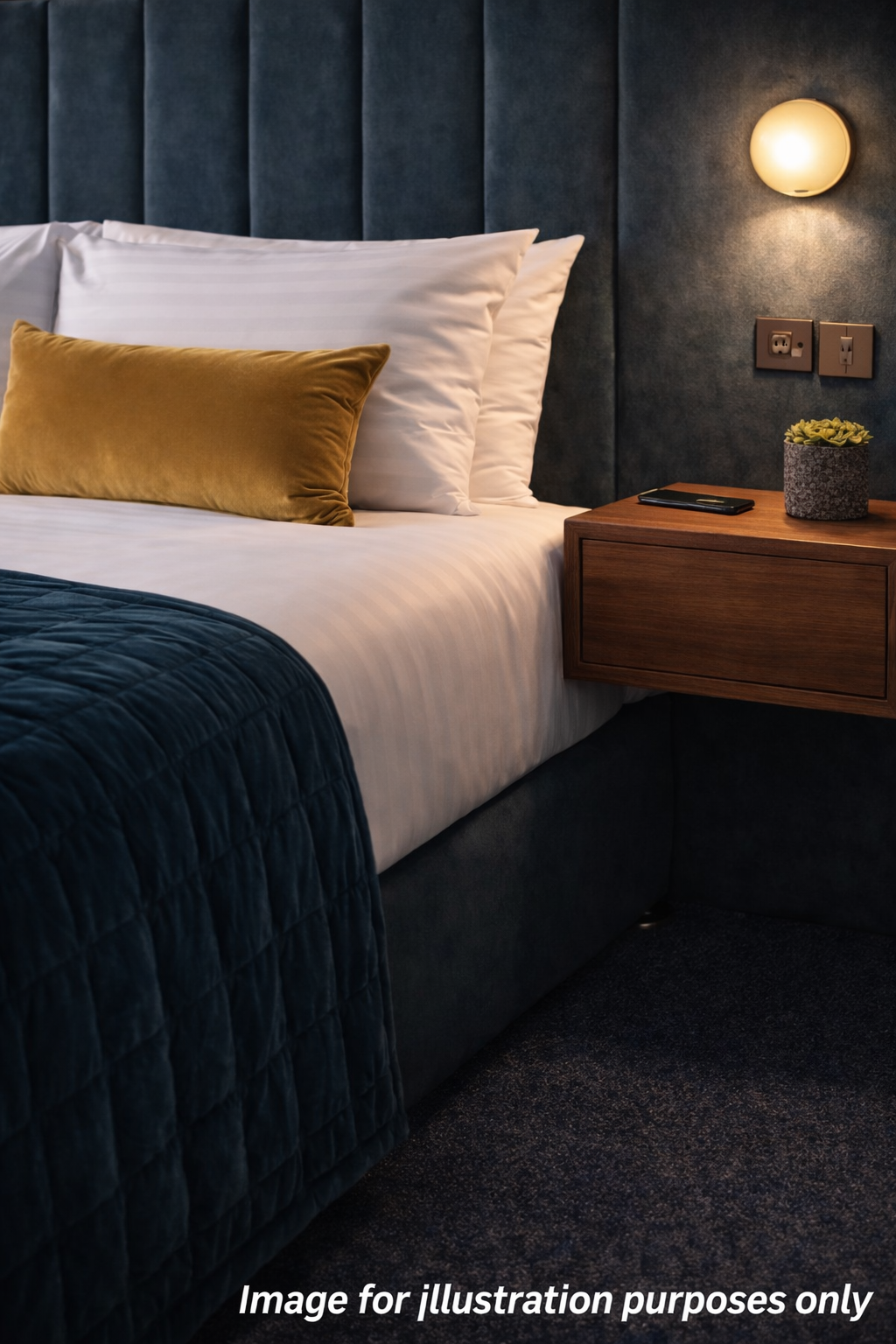 Bed with velvet cushion, wooden nightstand, and wall sconce in a hotel room.
