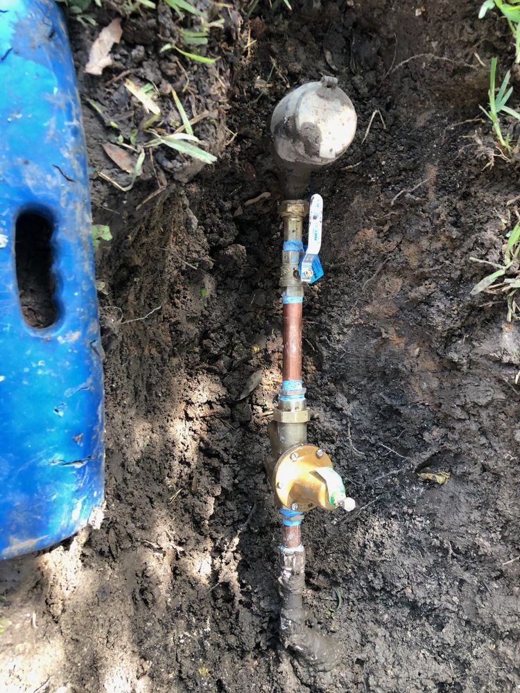 A water meter is sitting in the dirt next to a blue barrel.