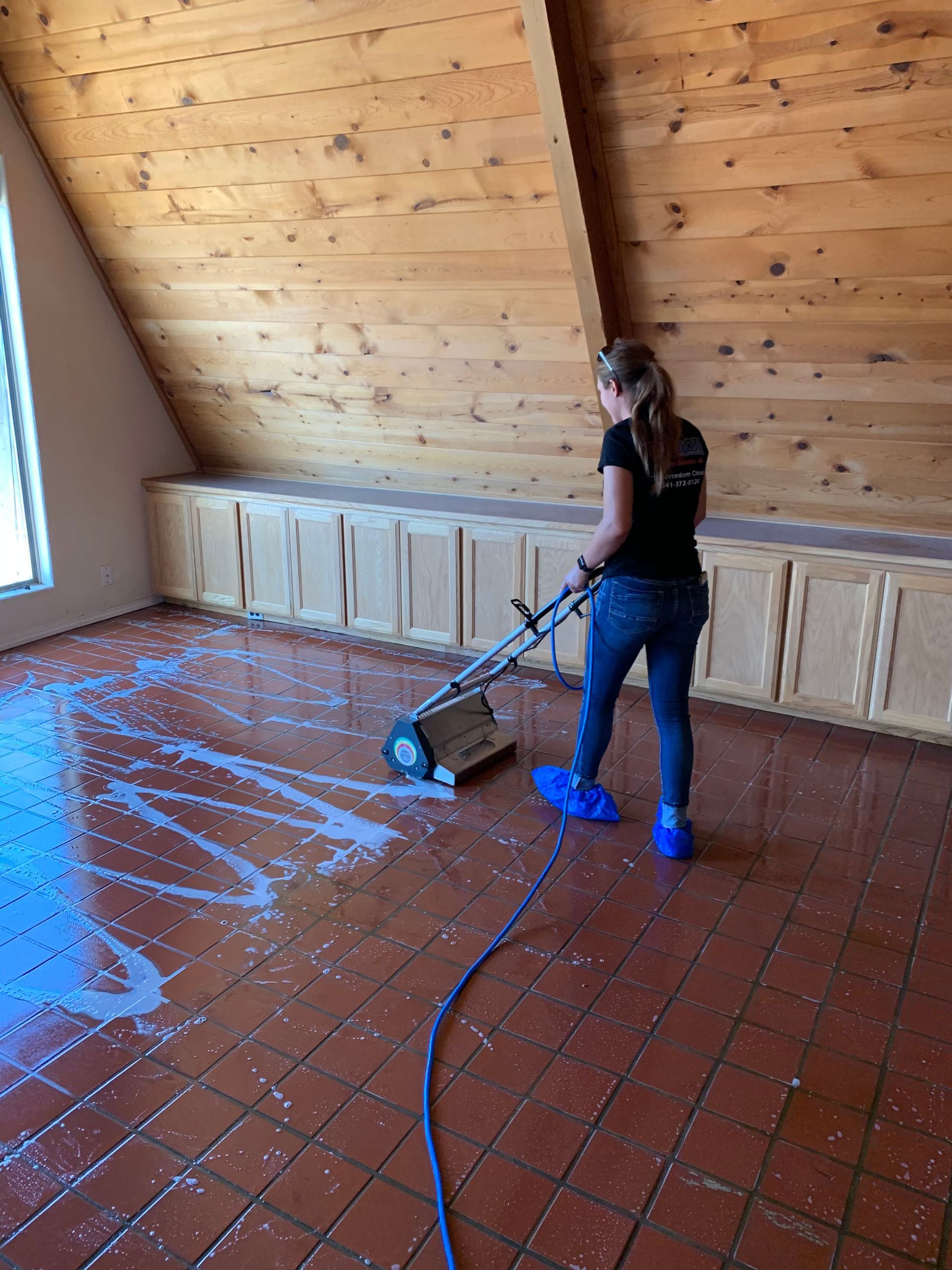 A woman is cleaning a tiled floor with a vacuum cleaner.