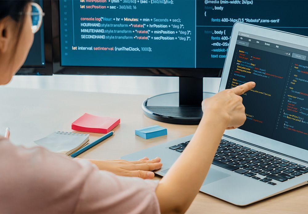 A woman is pointing at a laptop computer screen while sitting at a desk.