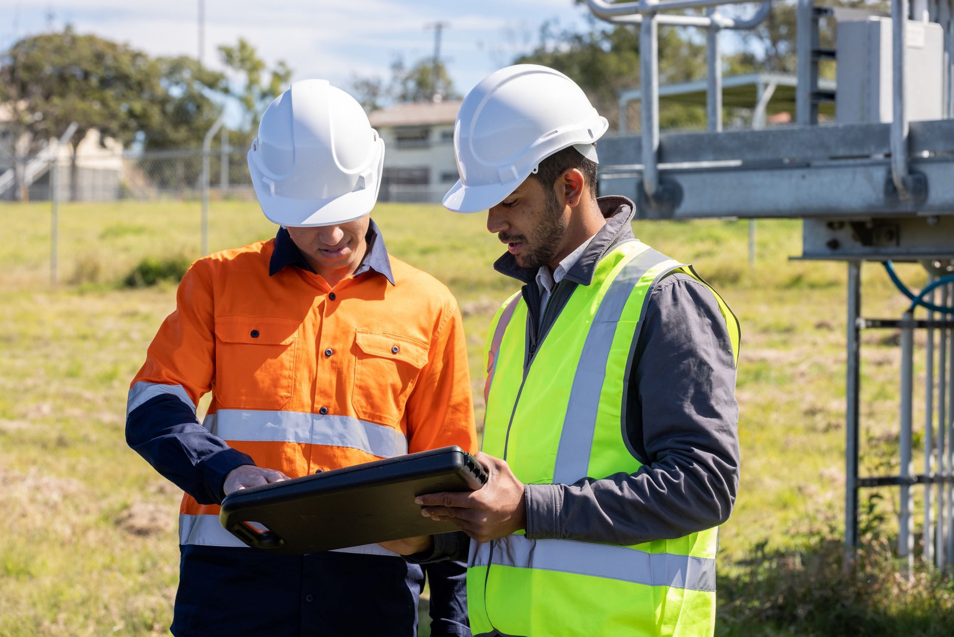 Two construction workers are looking at a laptop in a field.