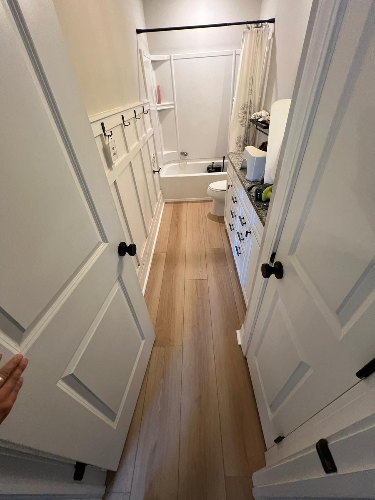 Narrow bathroom with white doors, walls, and flooring, and dark hardware.