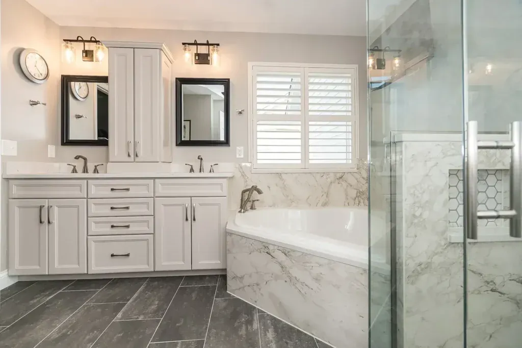 Gray and white bathroom with dual vanity, bathtub, and glass shower.