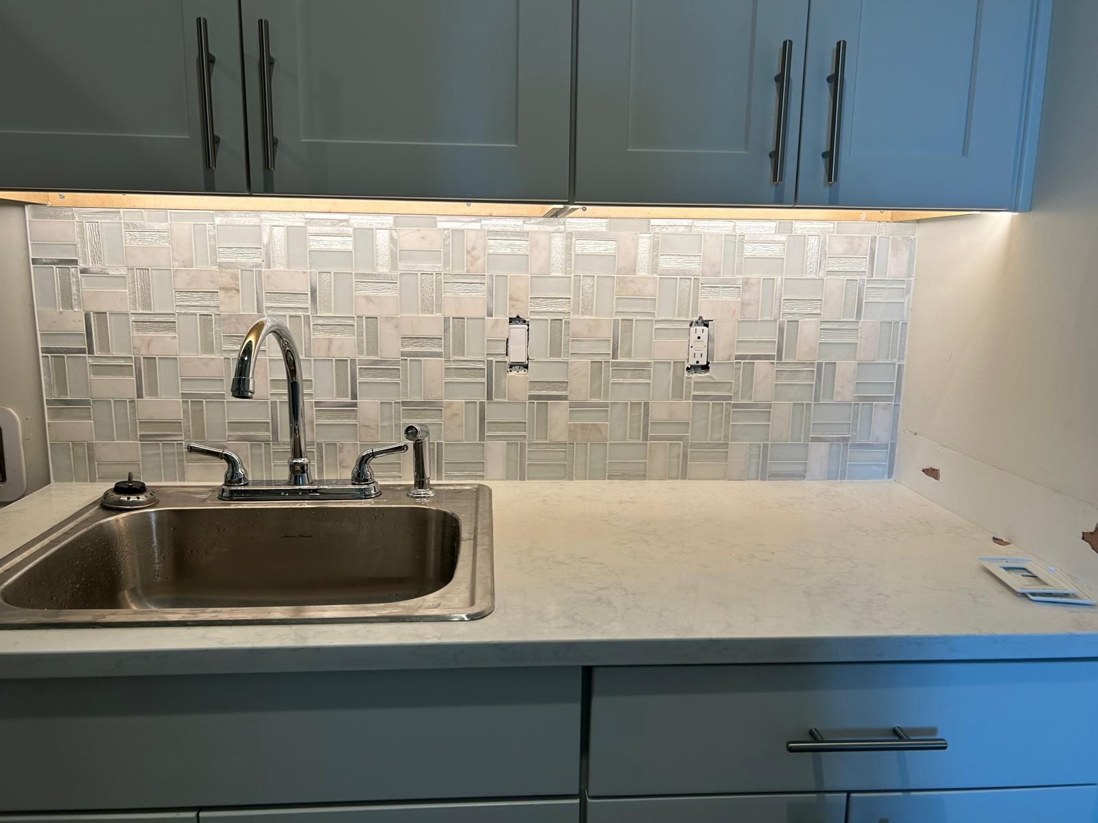 Kitchen sink with square, textured backsplash, light cabinets, and countertop.