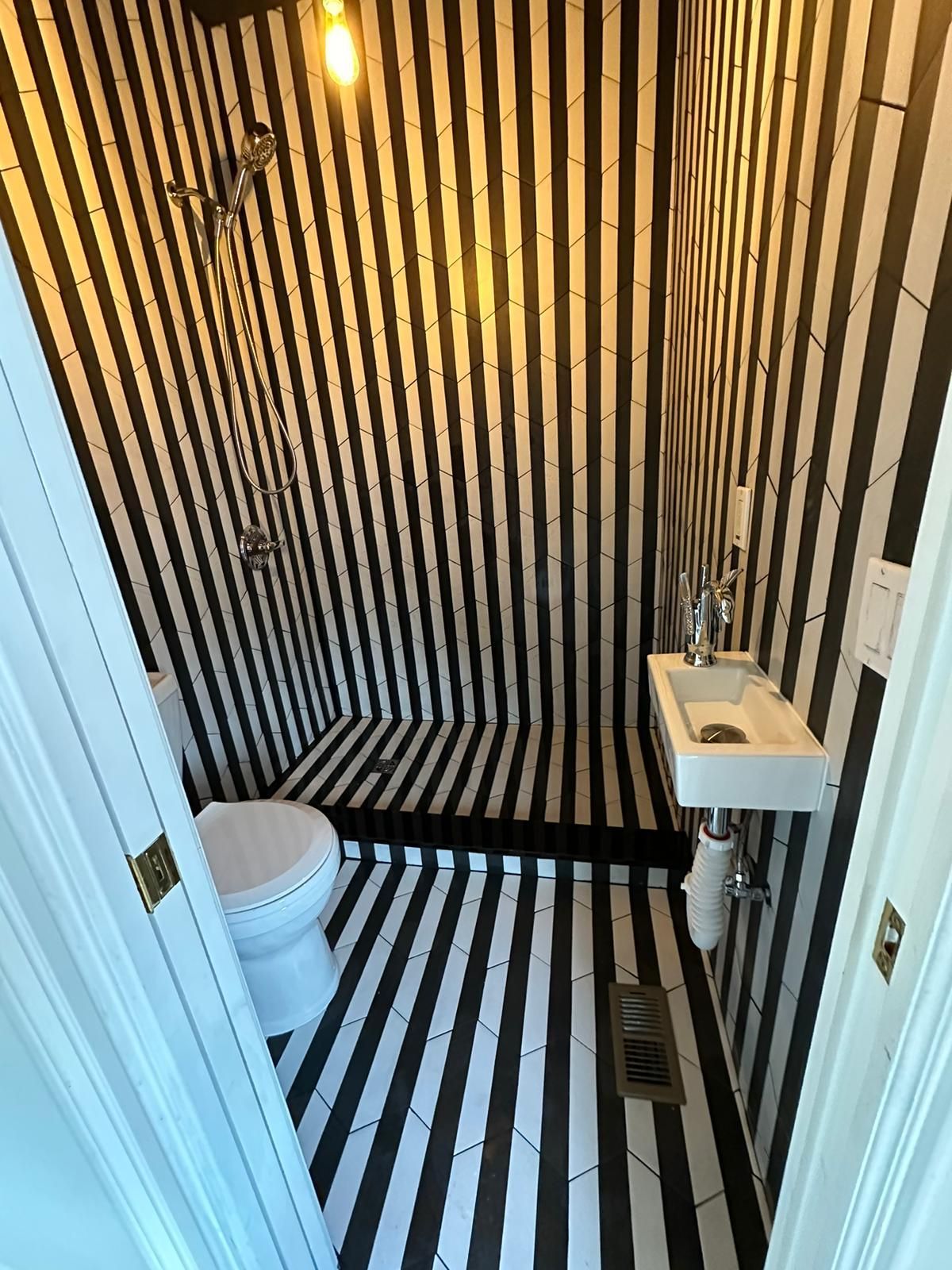 A small, black and white striped bathroom with a toilet, shower, and sink.