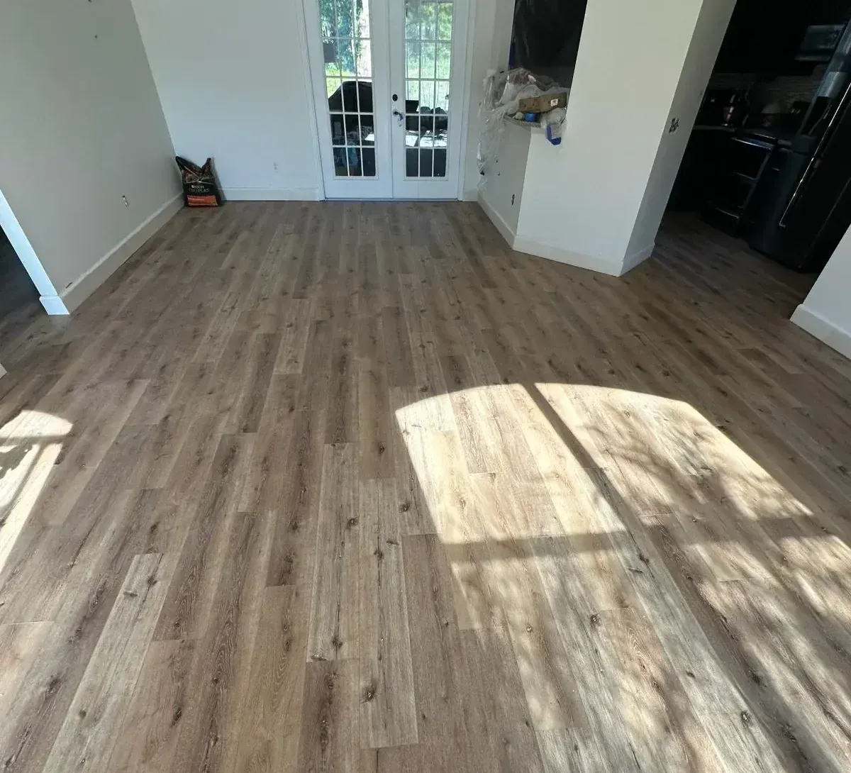 Light wood-look flooring in a room with white walls, french doors, and a shadow.