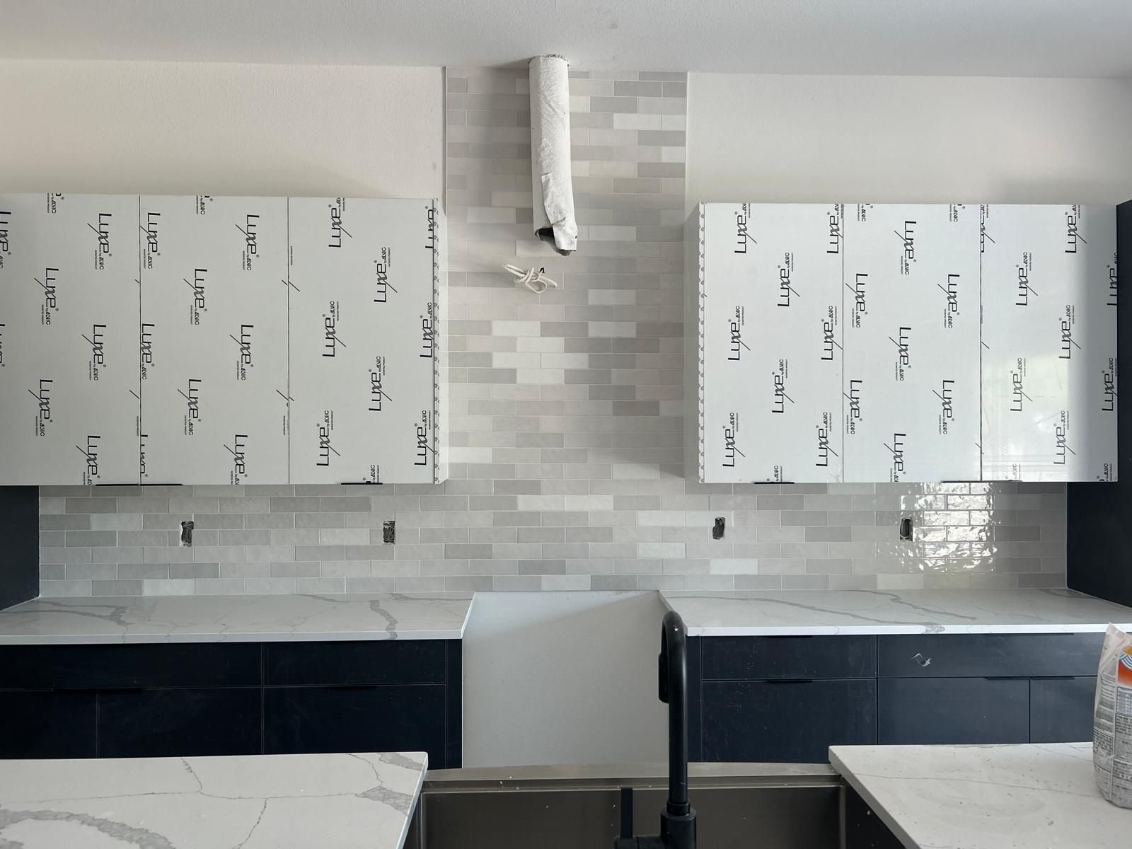 Kitchen with blue cabinets, white countertops, and grey brick-style backsplash. Cabinets have white protective film.