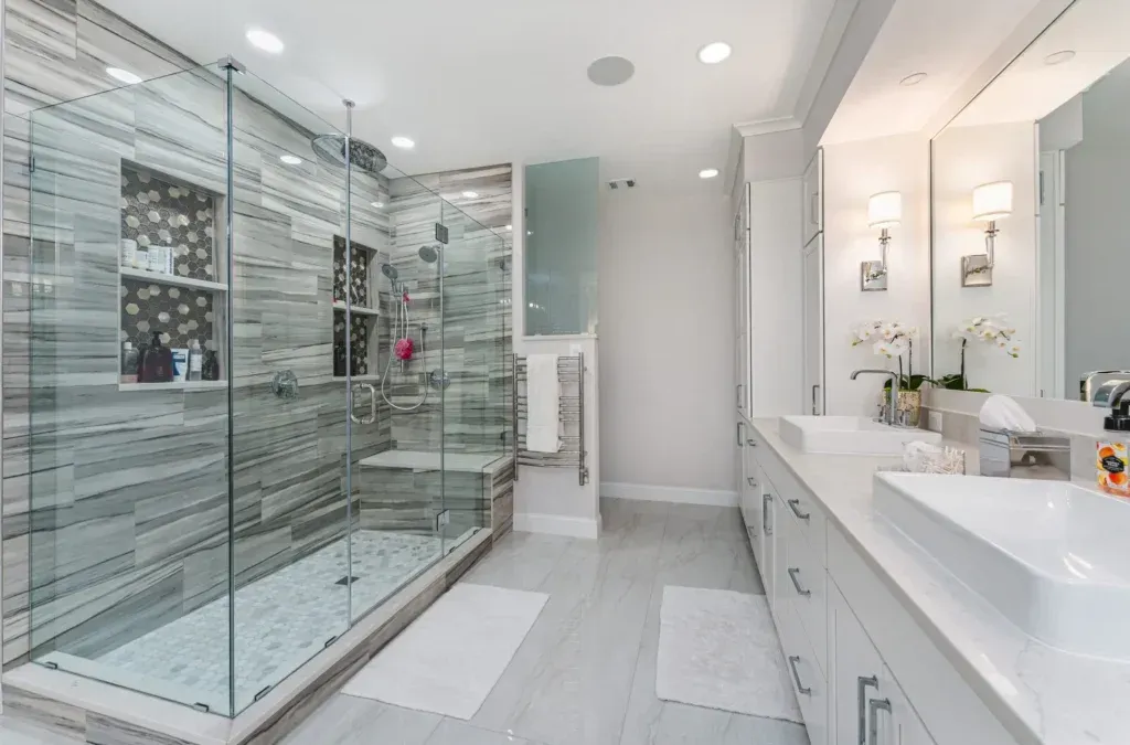 Spacious, bright bathroom with glass shower, double sinks, and white and gray tones.