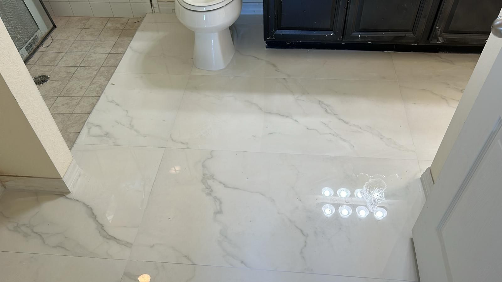 White marble bathroom floor with a toilet and dark cabinet.