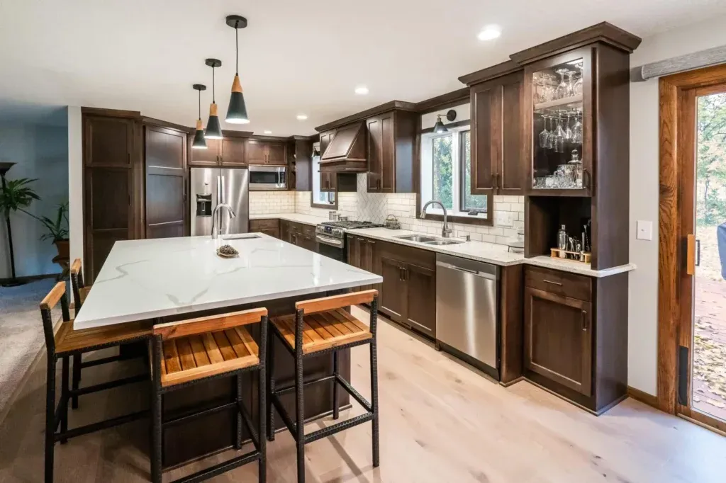 Modern kitchen with dark brown cabinets, white countertops, and wood floors. An island has seating.