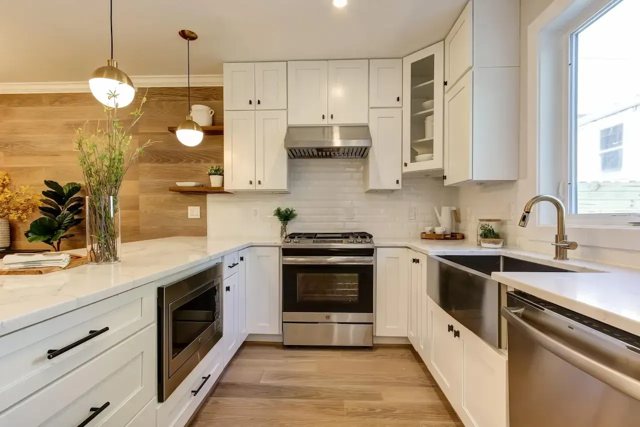 Modern U-shaped white kitchen with stainless steel appliances and light wood flooring.