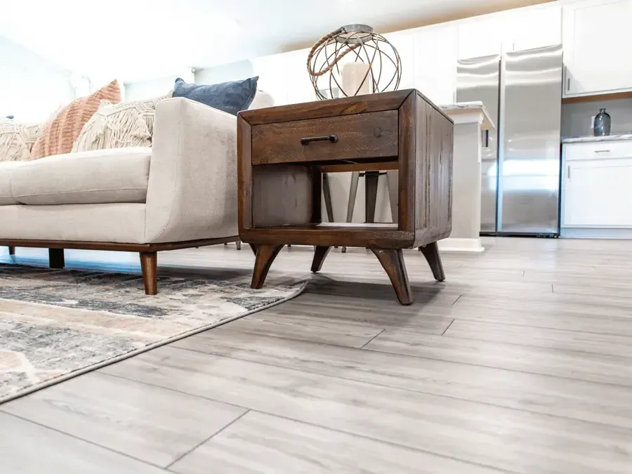Wooden nightstand next to a beige sofa on a light gray wood floor in a living room.