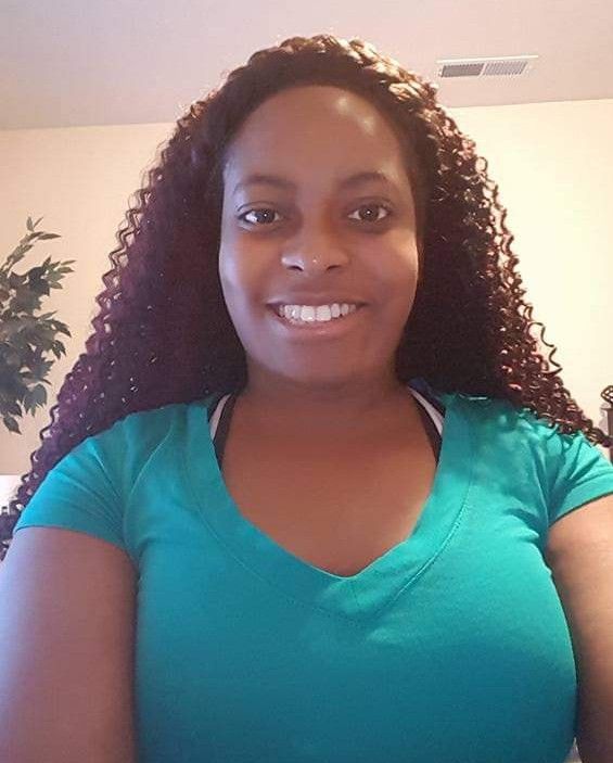 A woman with curly hair is wearing a green shirt and smiling.