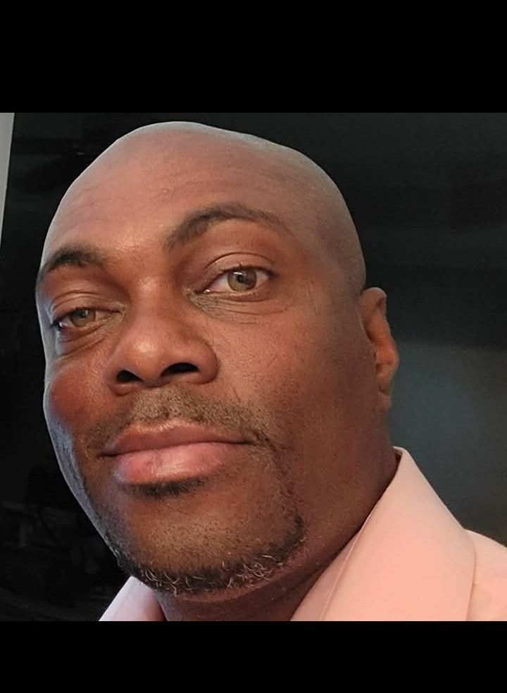 A bald man with a beard is wearing a pink shirt and looking at the camera.