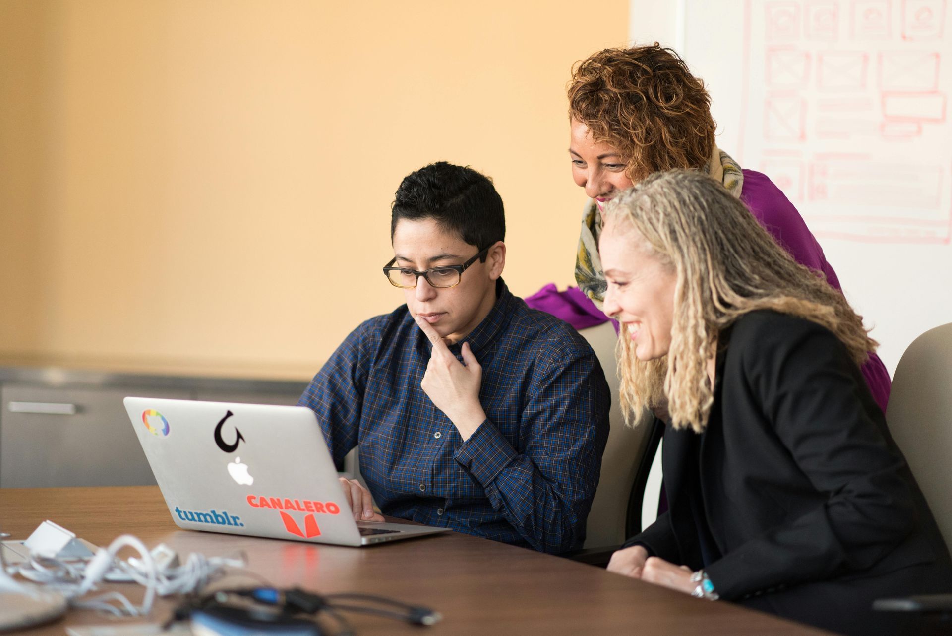 A group of people are sitting at a table looking at a laptop computer.