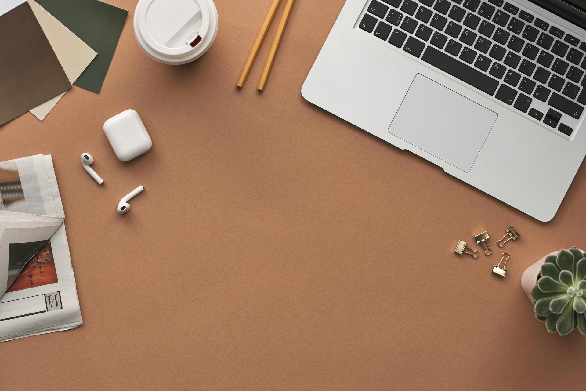 A desk with a laptop , headphones , a cup of coffee , and a plant.