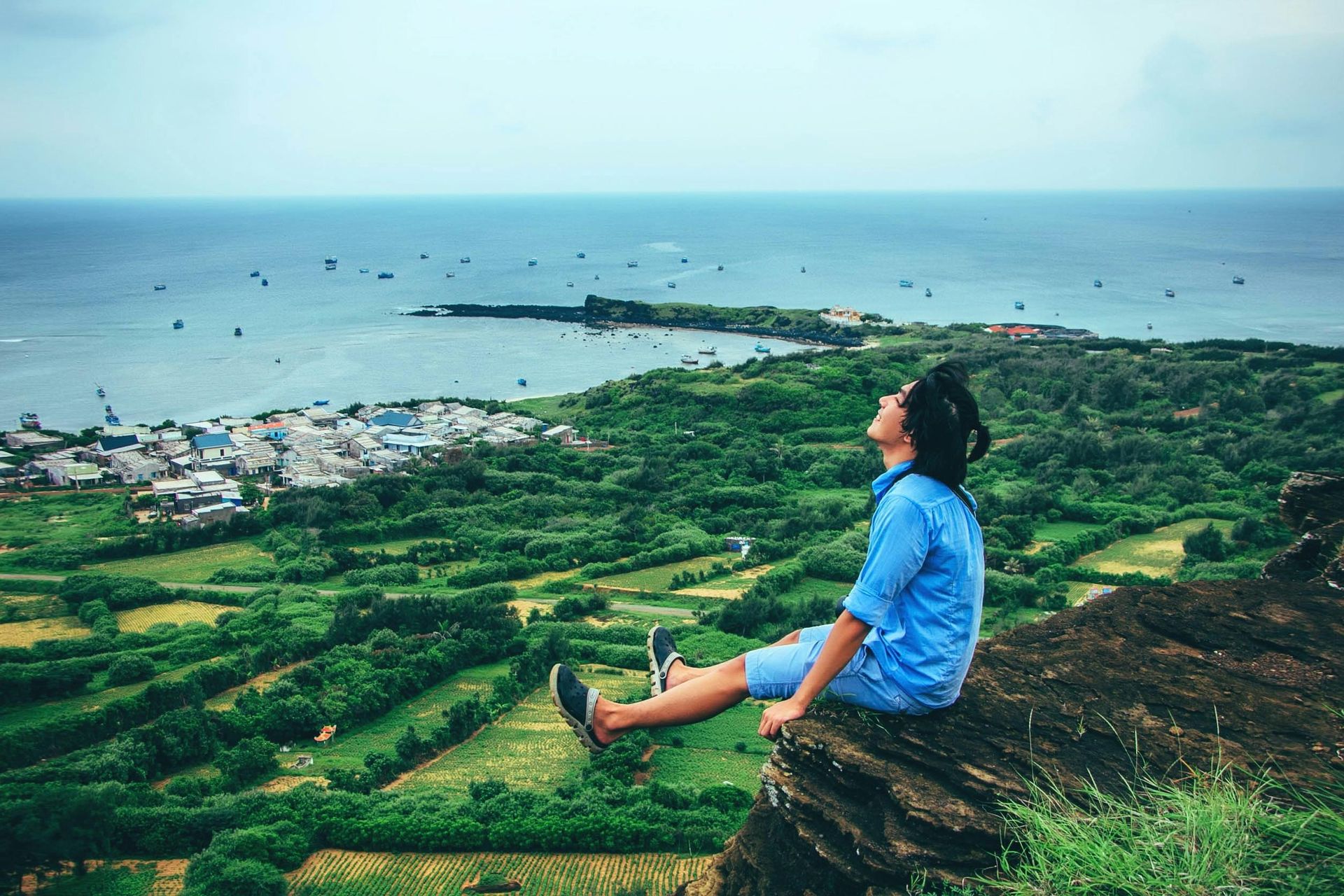 A man is sitting on the edge of a cliff overlooking the ocean.