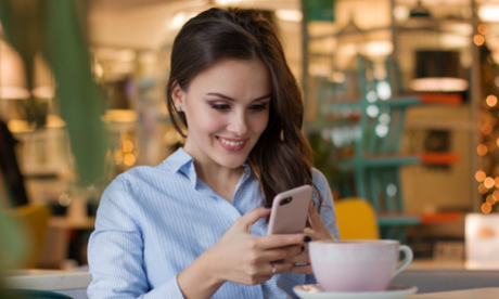 Smiling person in a blue shirt using a smartphone at a cafe table with a cup of coffee