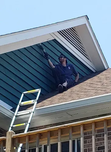 A man is sitting on the roof of a house with a ladder.