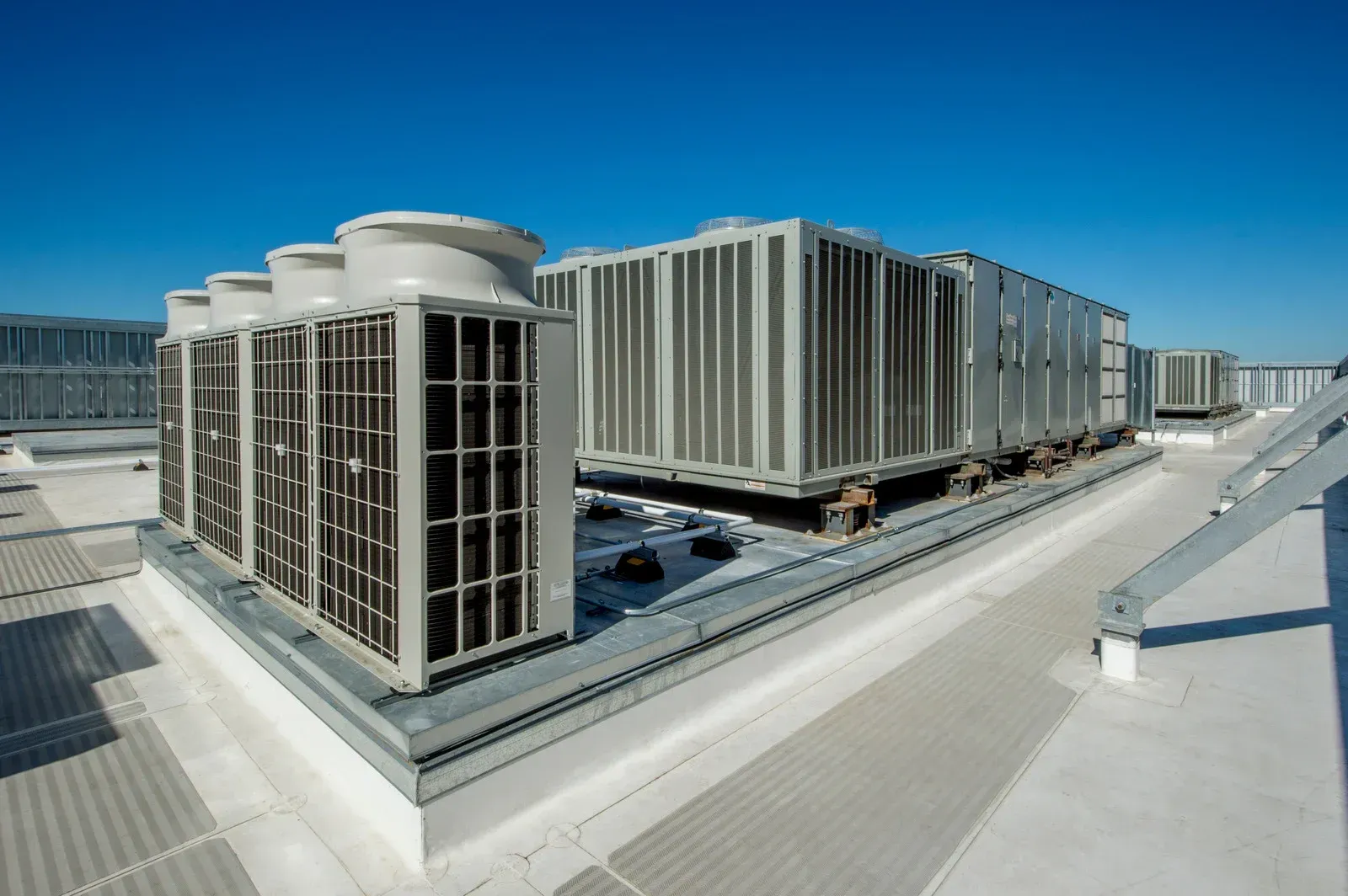 Industrial HVAC units and ventilation systems installed on a flat, gravel-covered roof against a clear blue sky.