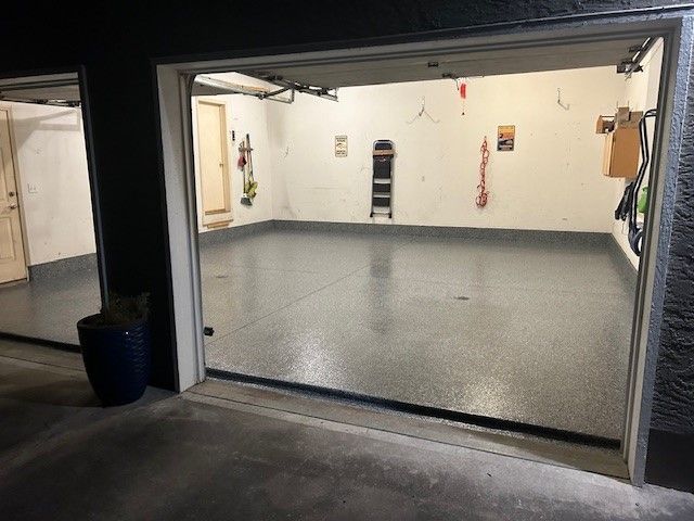 A garage with a gray floor and a white wall is open at night.