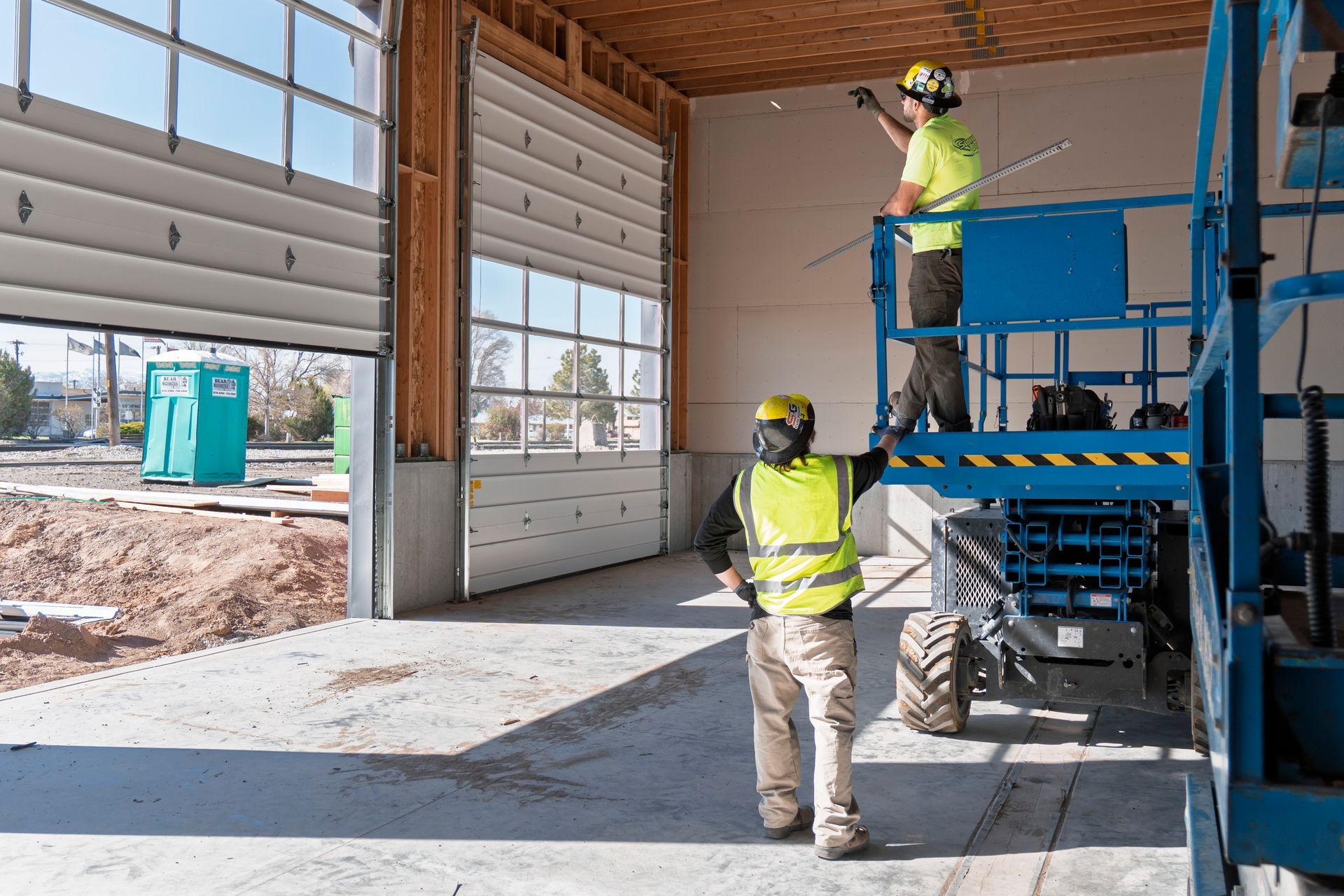 Two construction workers are working on a garage door.