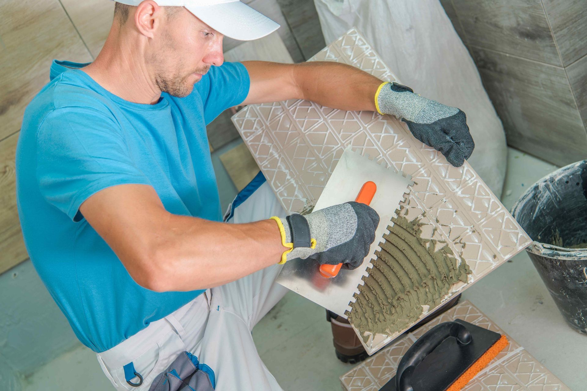 a man wearing gloves is using a trowel to apply adhesive to a tile