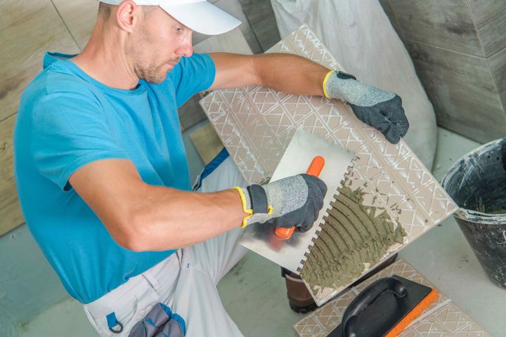 a man wearing gloves is using a trowel to apply adhesive to a tile
