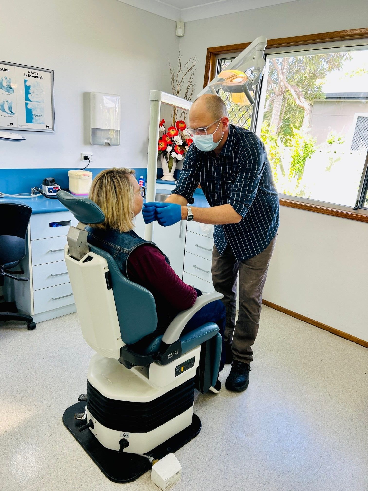 Dentist Wearing Mask Examines Seated Patient in a Bright Clinic Chair — Precise Dentures in Berserker, QLD