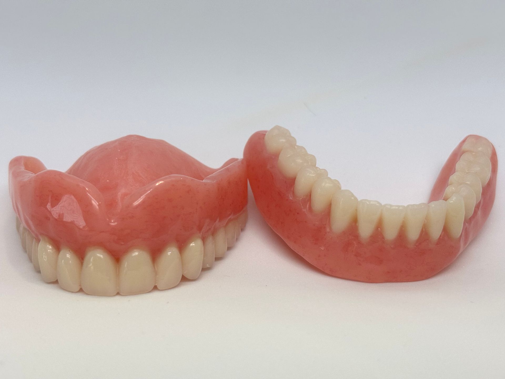 Two Pink Full Dentures on a White Background, One Front View and One Side View — Precise Dentures in Berserker, QLD