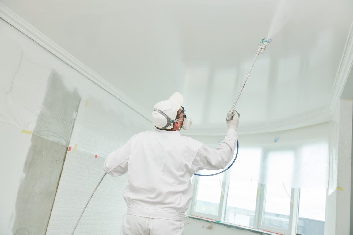 Painter spraying white paint on a ceiling in a bright room