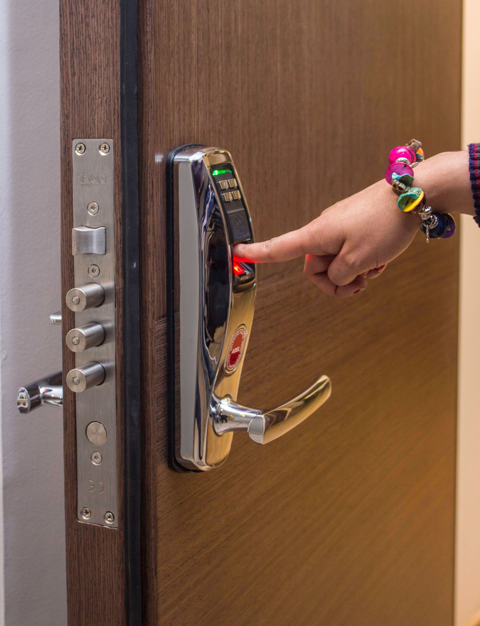 Hand pressing a glowing elevator call button on a wooden door panel