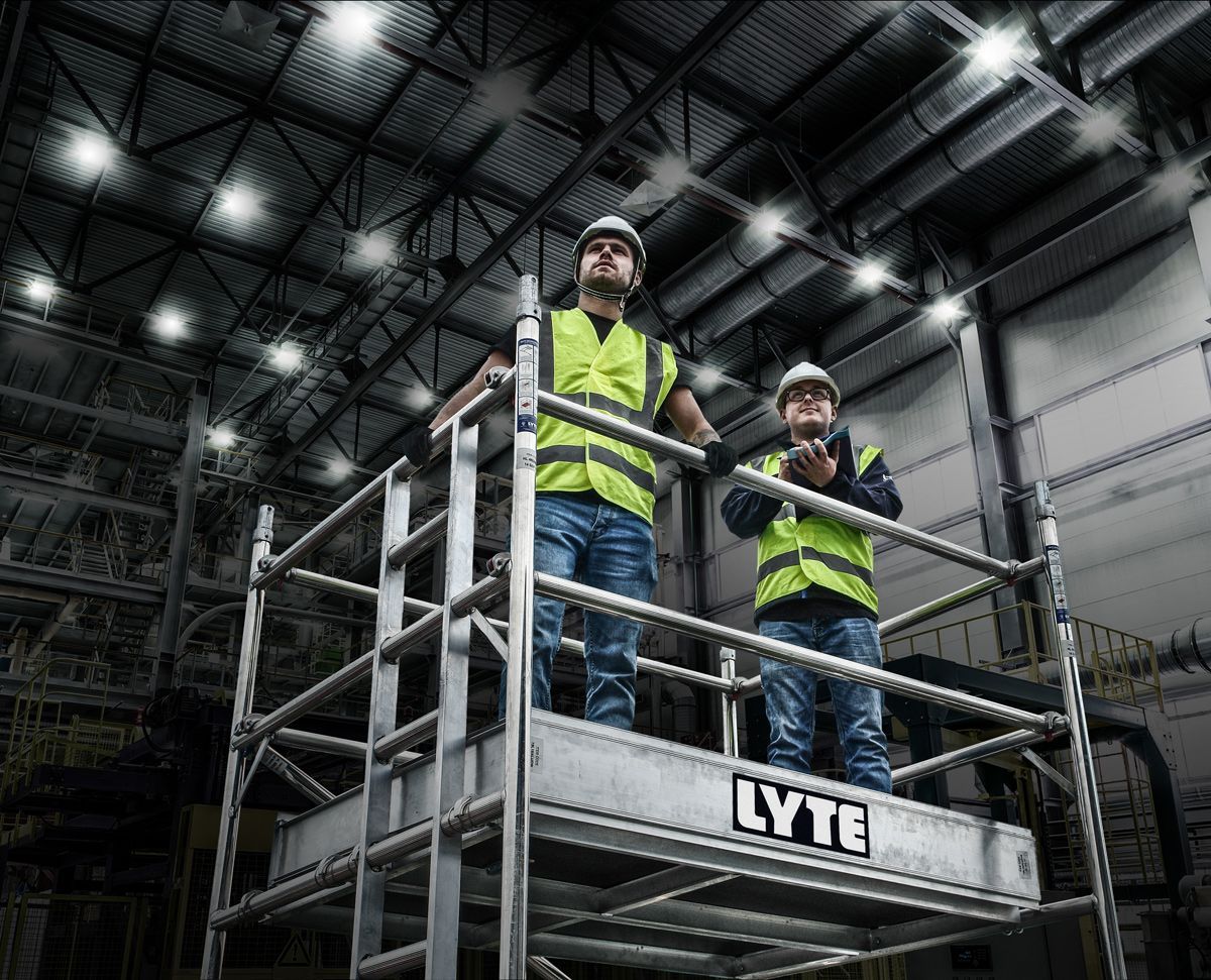 Two men are standing on a scaffolding in a warehouse.