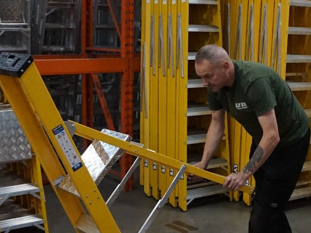 A man in a green shirt is pushing a yellow ladder