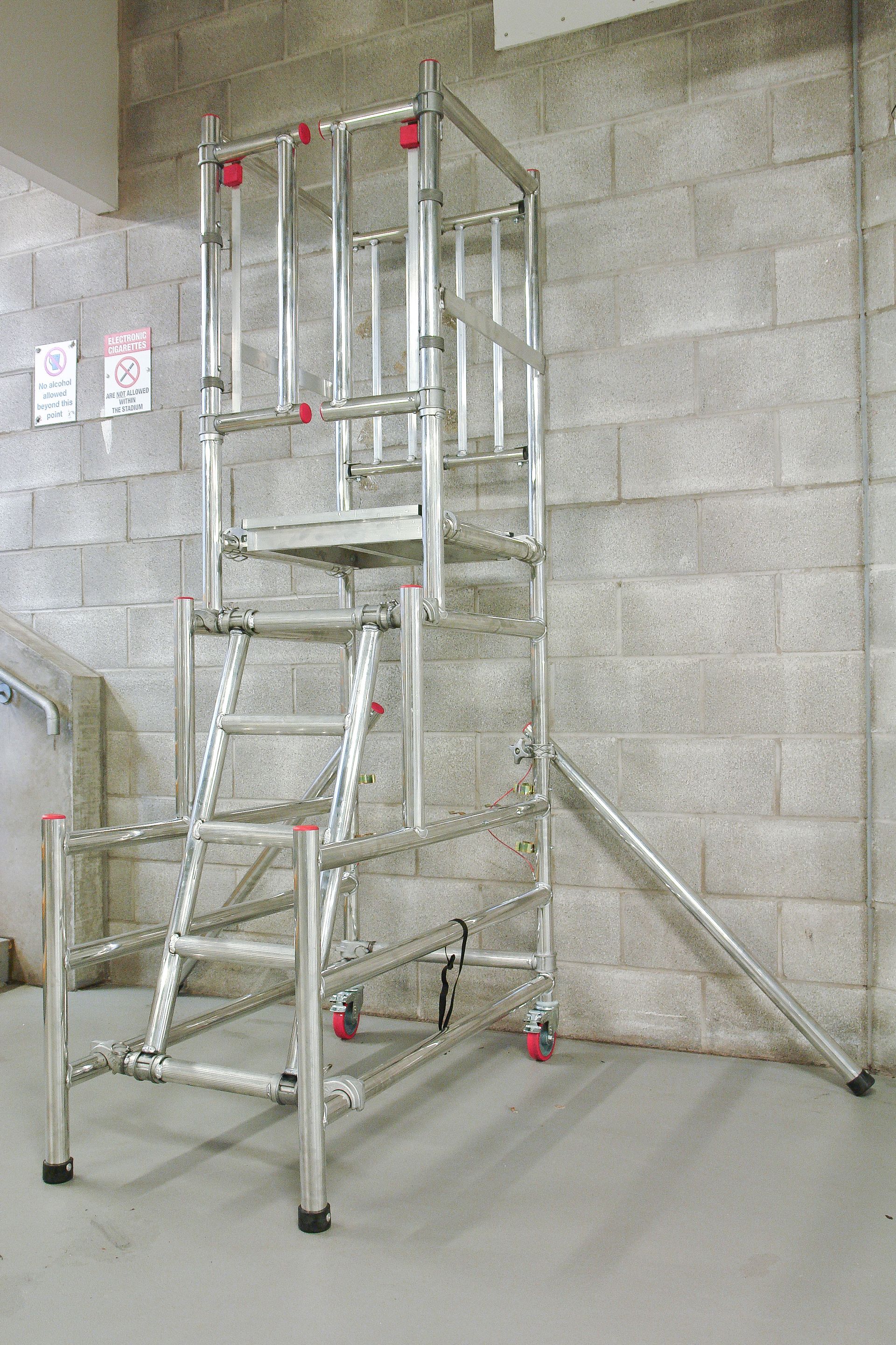 A metal ladder is sitting in front of a brick wall.