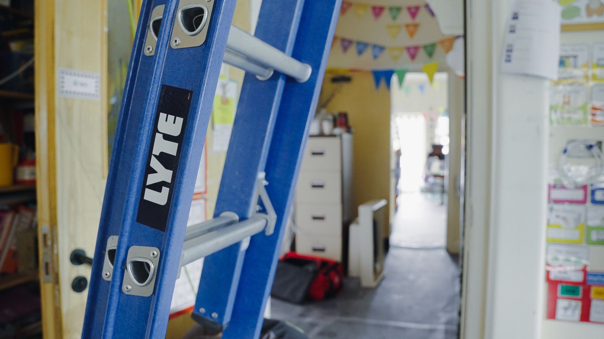 Blue fibreglass extension ladder being used in a school rewiring