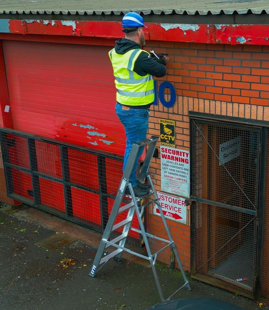 A man is standing on a ladder working on a camera installation.