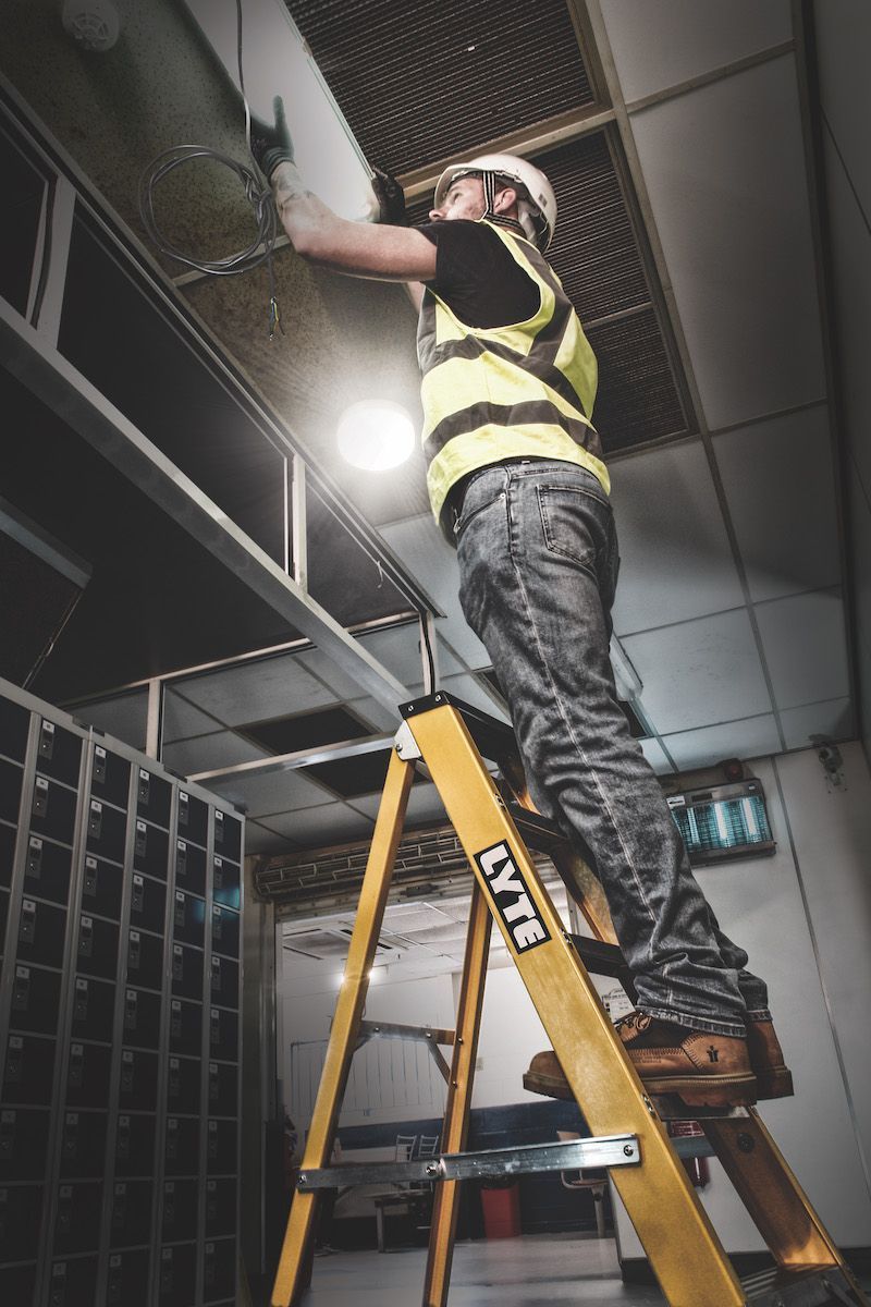 A man is standing on a ladder working on a ceiling.