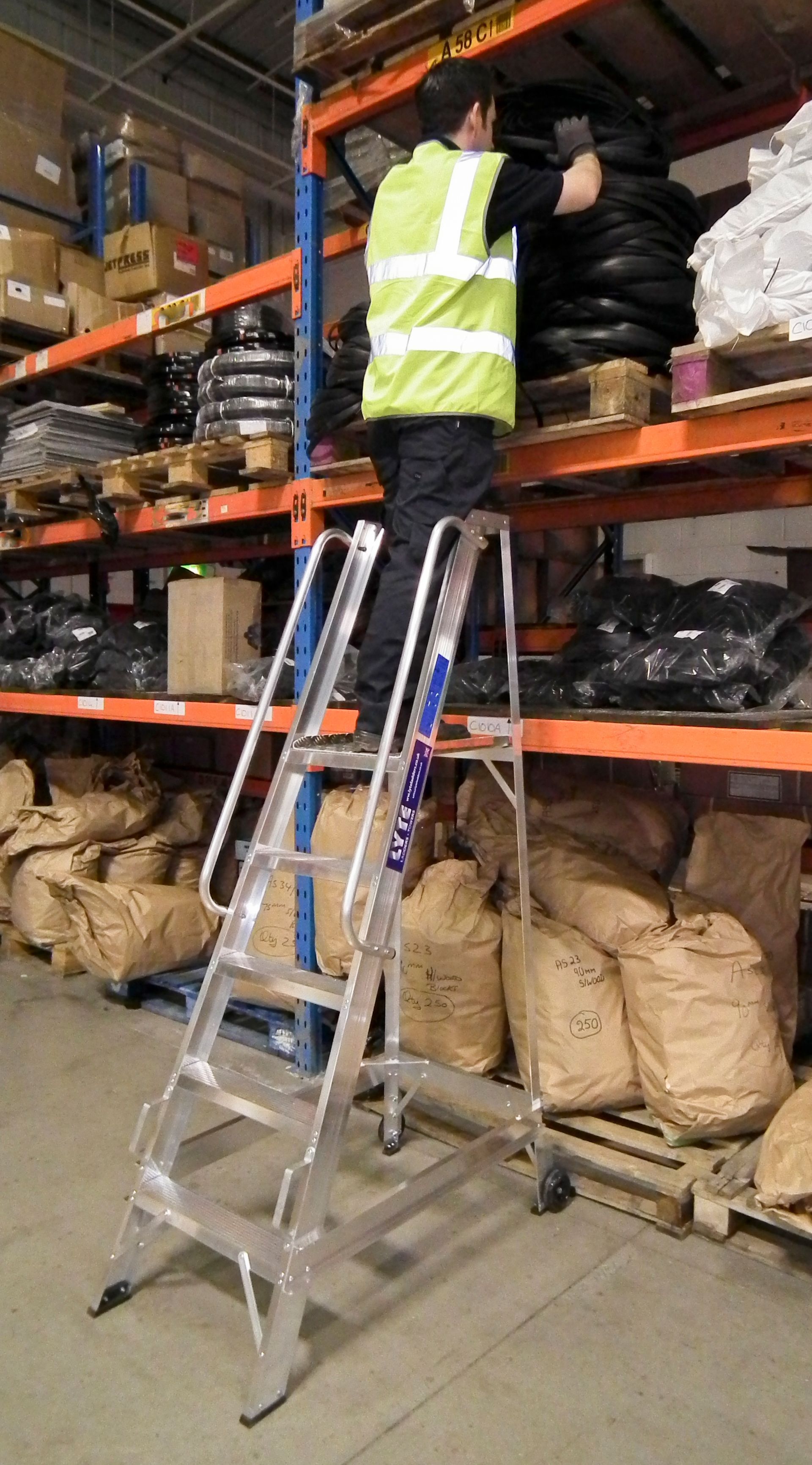 A man is standing on a ladder in a warehouse.