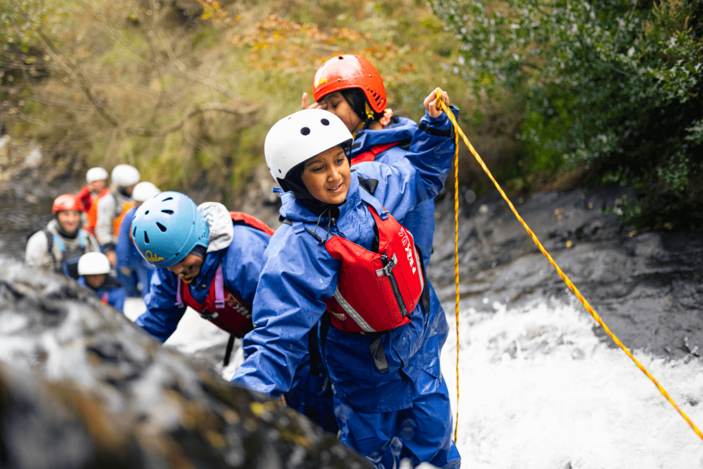 A group of people are climbing a waterfall with a rope.